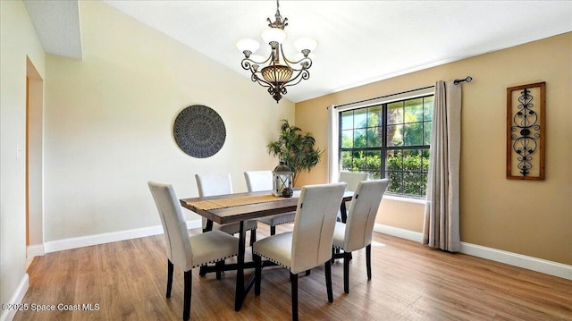 dining room featuring lofted ceiling, light wood-style flooring, a notable chandelier, and baseboards