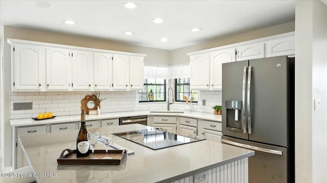 kitchen featuring a sink, a kitchen island, stainless steel appliances, white cabinets, and decorative backsplash