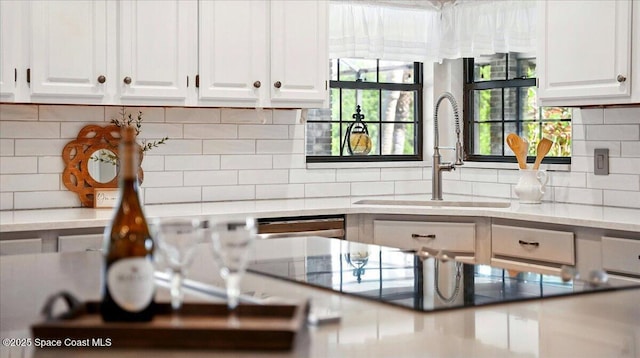 kitchen featuring a sink, stainless steel dishwasher, white cabinets, decorative backsplash, and black electric stovetop