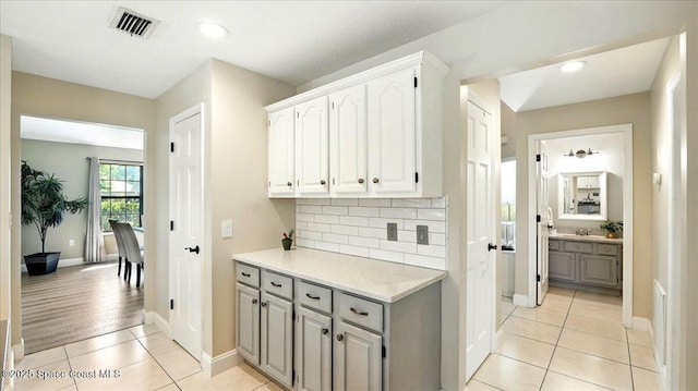 corridor featuring light tile patterned floors, baseboards, visible vents, and a sink