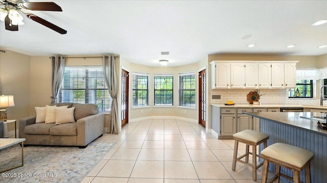 kitchen featuring backsplash, white cabinets, light tile patterned floors, baseboards, and ceiling fan