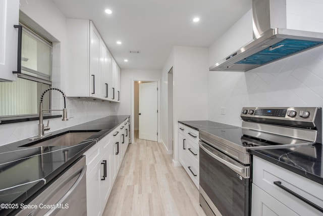 kitchen with wall chimney range hood, appliances with stainless steel finishes, light wood-style floors, white cabinets, and a sink