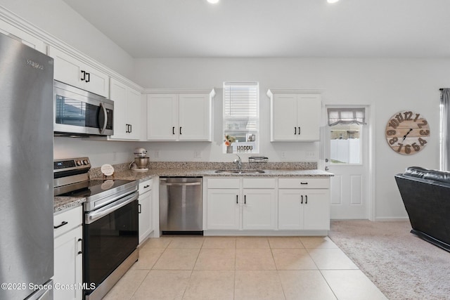 kitchen featuring light stone countertops, appliances with stainless steel finishes, light tile patterned flooring, white cabinetry, and a sink