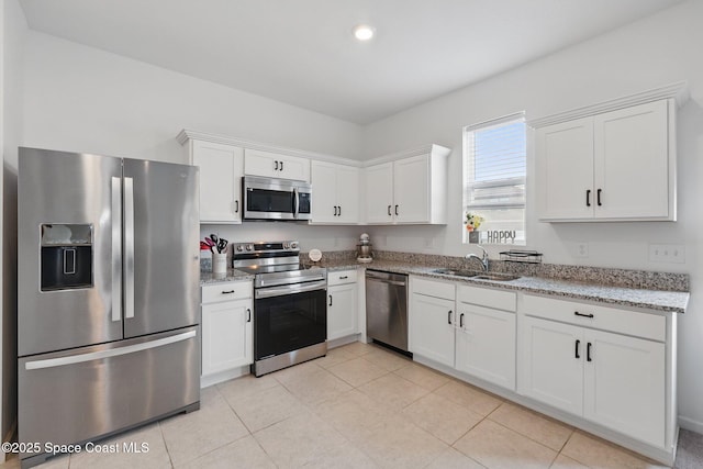 kitchen with light stone counters, appliances with stainless steel finishes, light tile patterned flooring, white cabinets, and a sink