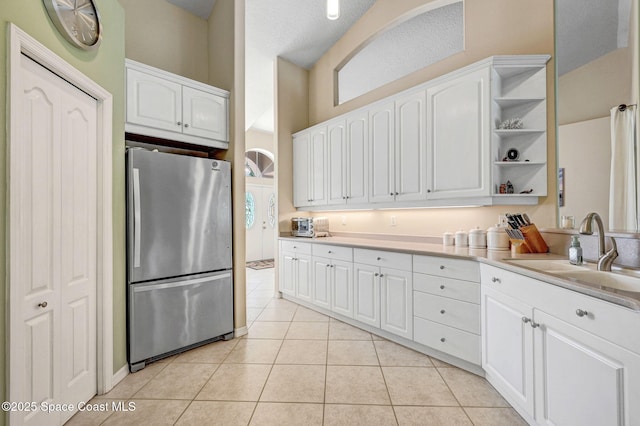 kitchen featuring open shelves, light tile patterned flooring, freestanding refrigerator, a sink, and white cabinets