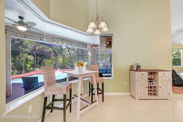 dining area featuring tile patterned flooring, ceiling fan with notable chandelier, baseboards, and a sunroom