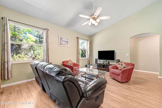 living room featuring lofted ceiling, baseboards, arched walkways, and light wood finished floors