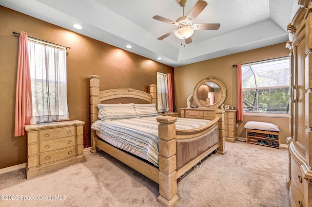 bedroom with a ceiling fan, a tray ceiling, light colored carpet, and baseboards