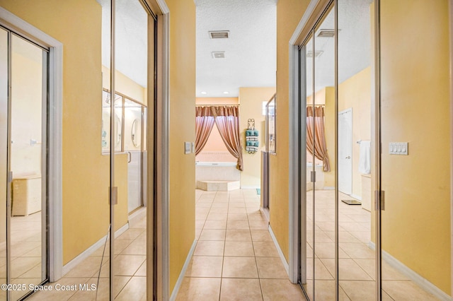 hallway featuring light tile patterned floors, visible vents, baseboards, and a textured ceiling