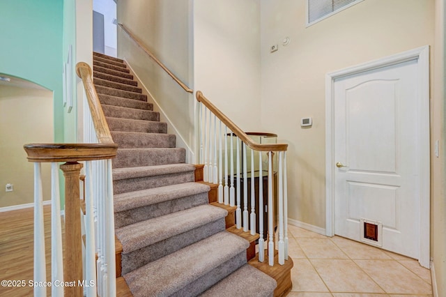 staircase featuring tile patterned floors, visible vents, baseboards, and arched walkways