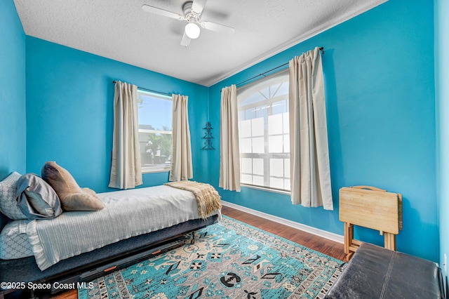 bedroom with a textured ceiling, a ceiling fan, baseboards, and wood finished floors