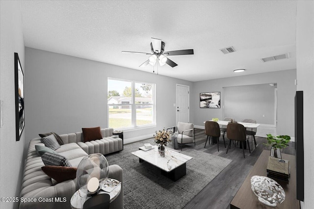 living room featuring visible vents, a textured ceiling, baseboards, and wood finished floors