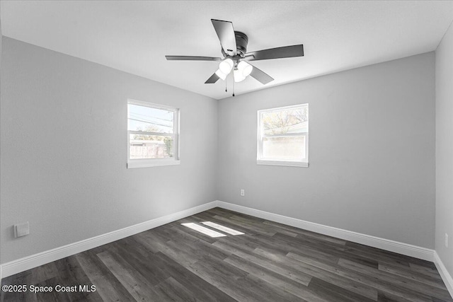 spare room featuring a wealth of natural light, dark wood finished floors, a ceiling fan, and baseboards