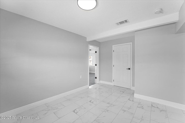 spare room with visible vents, baseboards, marble finish floor, and a textured ceiling