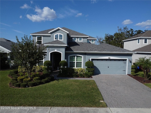 traditional-style house with a front yard, roof with shingles, stucco siding, decorative driveway, and an attached garage