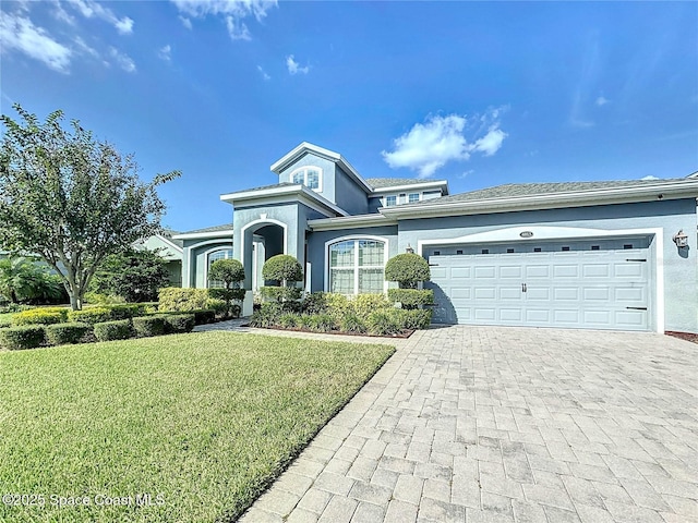 view of front of home featuring a front yard, decorative driveway, an attached garage, and stucco siding