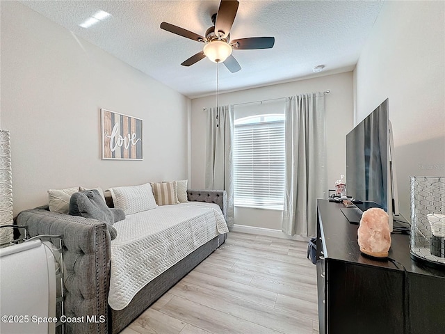 bedroom with ceiling fan, baseboards, light wood finished floors, and a textured ceiling