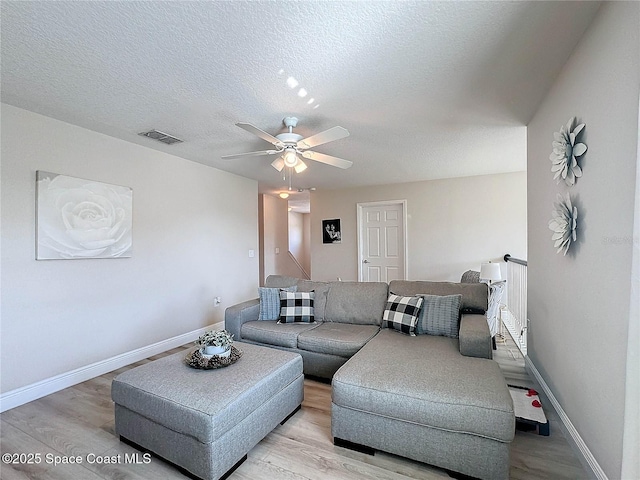 living area with visible vents, a textured ceiling, baseboards, and light wood-style floors