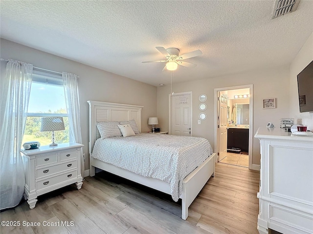 bedroom featuring visible vents, ensuite bath, light wood-style flooring, and a ceiling fan