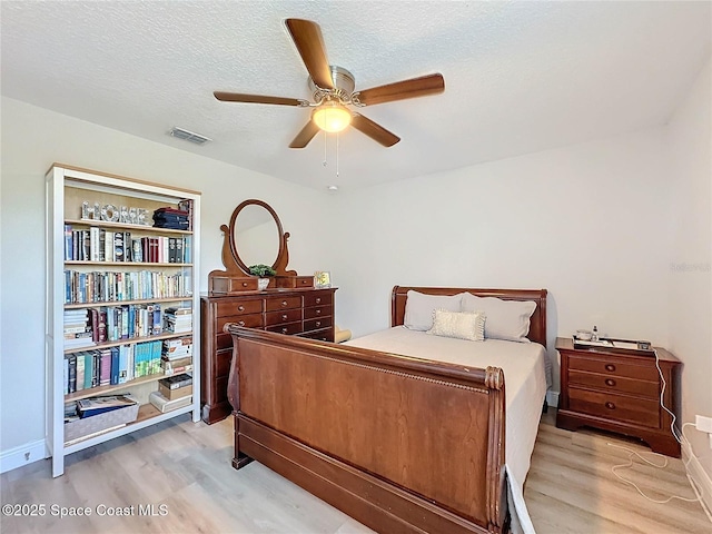 bedroom featuring light wood finished floors, visible vents, a textured ceiling, and ceiling fan