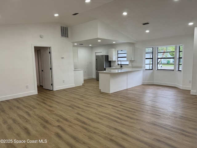 kitchen featuring visible vents, open floor plan, a peninsula, freestanding refrigerator, and white cabinets