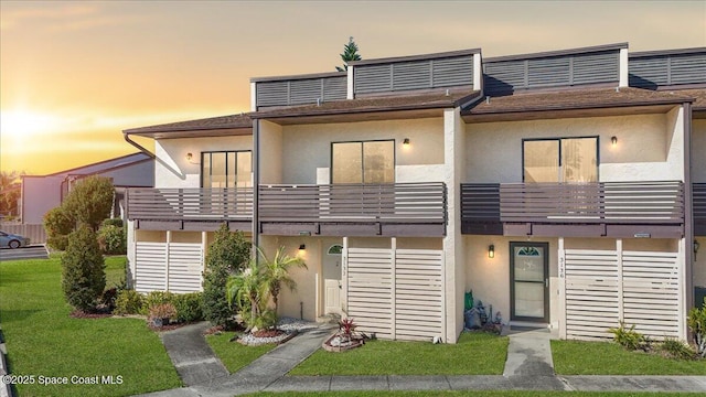 view of front of house with a balcony, stucco siding, and a front yard