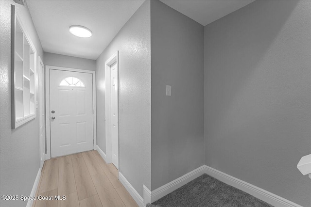 doorway to outside featuring light wood-type flooring, baseboards, and a textured wall