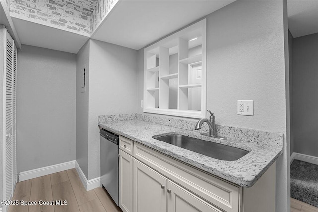 kitchen featuring a sink, light stone counters, stainless steel dishwasher, light wood finished floors, and baseboards