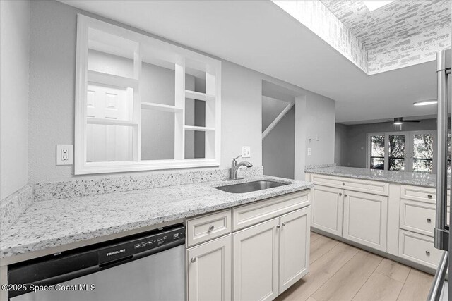 kitchen with light stone counters, white cabinetry, light wood finished floors, a sink, and dishwasher