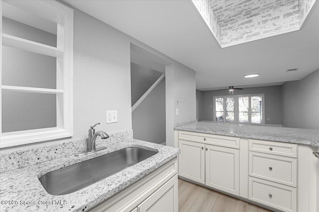 kitchen with light stone countertops, light wood-style flooring, ceiling fan, a sink, and white cabinets