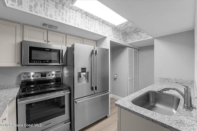 kitchen with visible vents, light wood-style flooring, a sink, appliances with stainless steel finishes, and light stone countertops