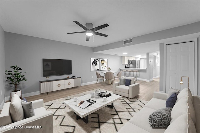 living room with a ceiling fan, light wood-style floors, visible vents, and baseboards