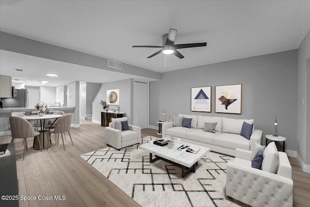 living room featuring light wood-style flooring, baseboards, visible vents, and ceiling fan