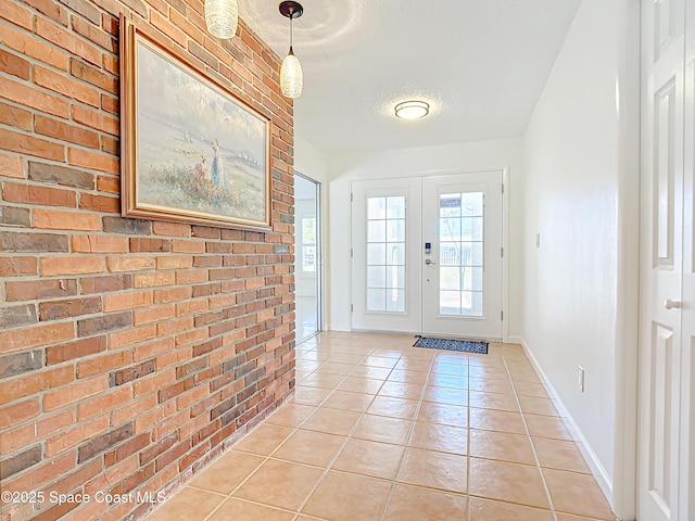 doorway to outside with a textured ceiling, french doors, brick wall, light tile patterned flooring, and baseboards