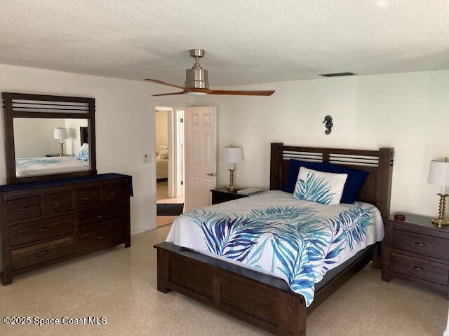 bedroom with visible vents, light speckled floor, a textured ceiling, and a ceiling fan