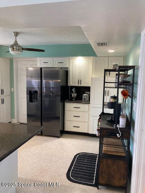 kitchen featuring visible vents, ceiling fan, black fridge with ice dispenser, white cabinetry, and dark countertops