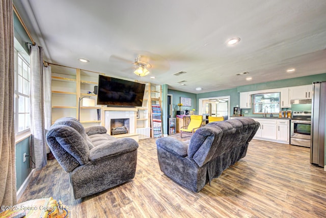 living room with a glass covered fireplace, recessed lighting, wood finished floors, and ceiling fan