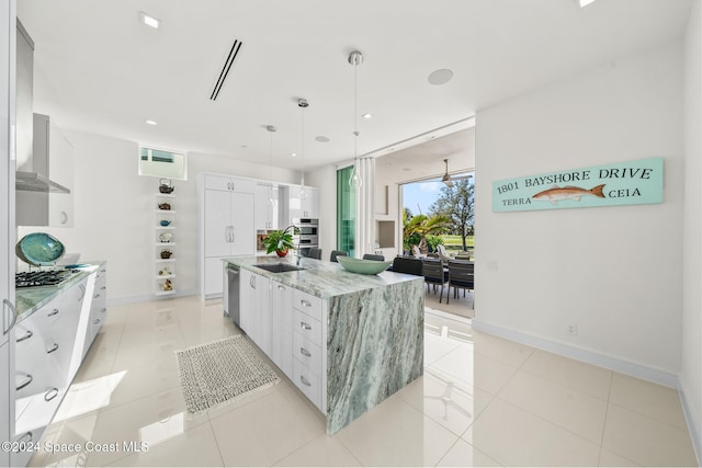 kitchen featuring light tile patterned floors, stainless steel appliances, an island with sink, and white cabinetry