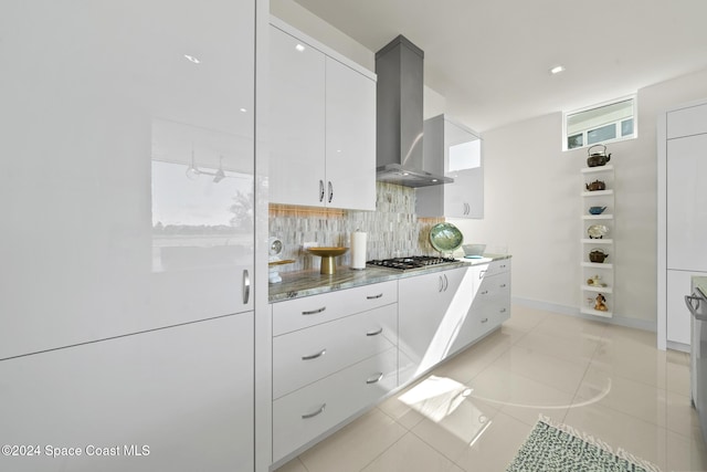 kitchen featuring stainless steel gas cooktop, light tile patterned floors, decorative backsplash, white cabinets, and wall chimney exhaust hood