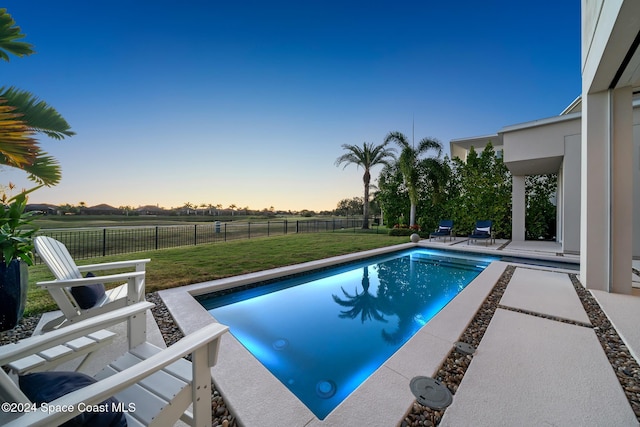 pool at dusk with a fenced backyard, a fenced in pool, a patio, and a yard