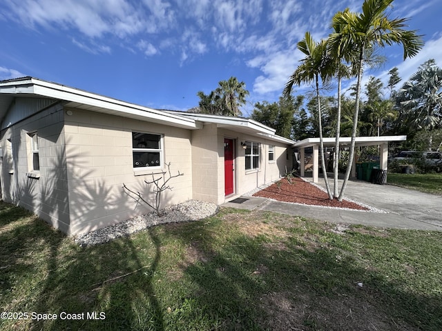 view of front of property with concrete block siding, a carport, and a front lawn