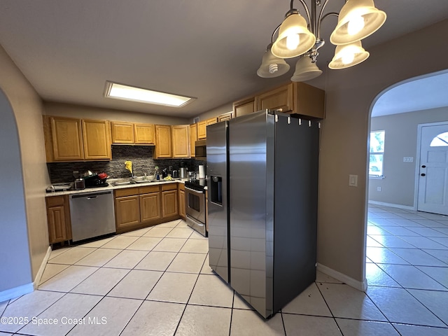 kitchen featuring arched walkways, appliances with stainless steel finishes, light countertops, light tile patterned floors, and decorative backsplash