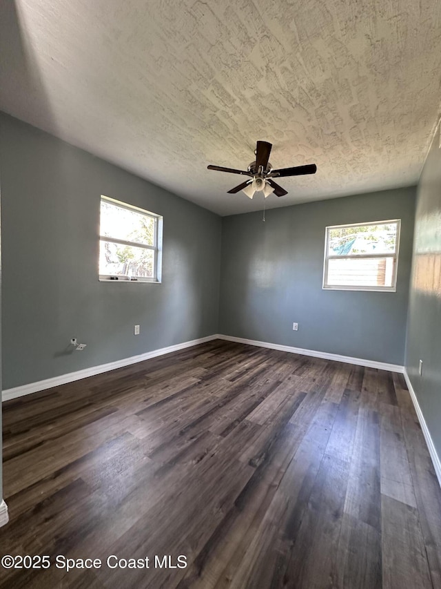 spare room featuring plenty of natural light, a ceiling fan, dark wood-type flooring, and baseboards