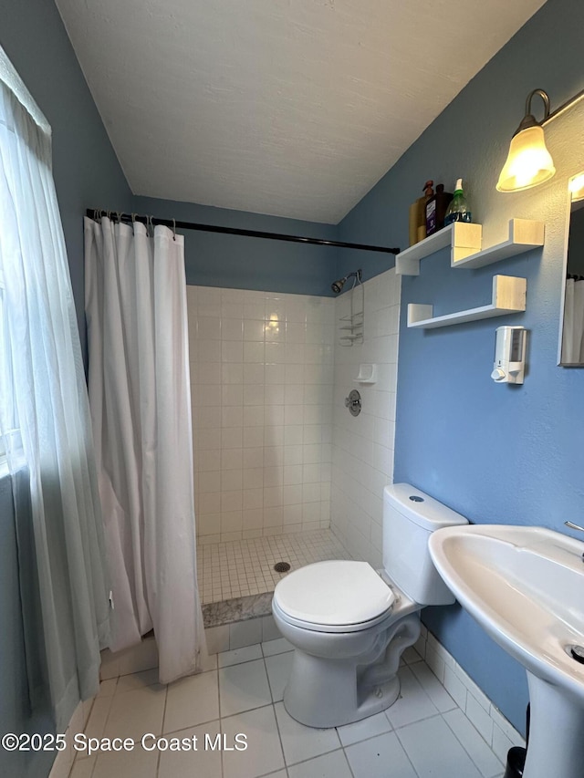 bathroom with a tile shower, tile patterned floors, toilet, and a sink