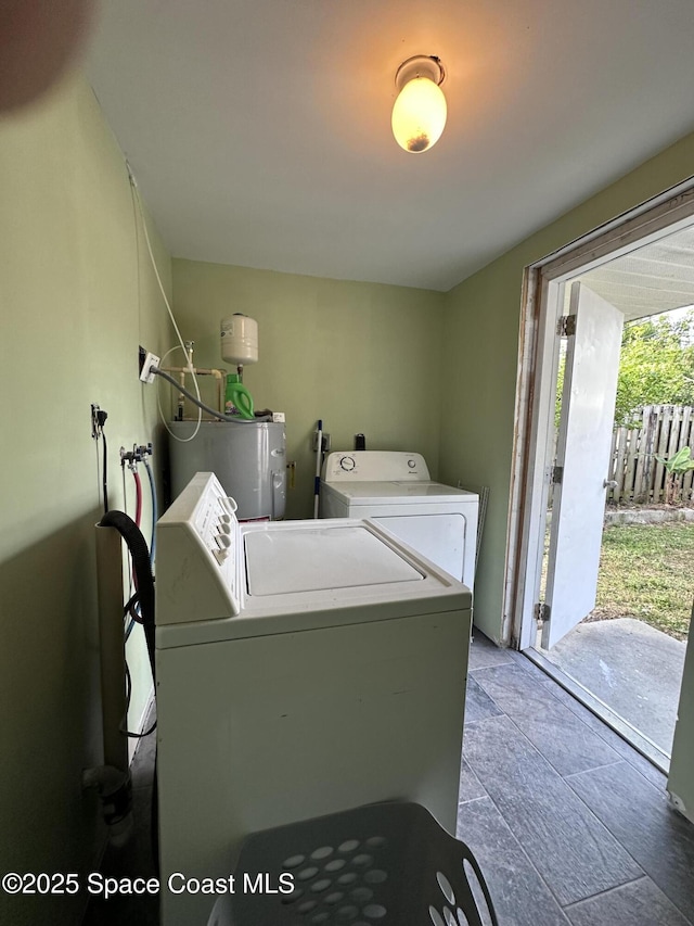 clothes washing area featuring water heater, laundry area, stone finish floor, and separate washer and dryer