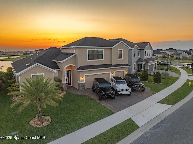 view of front facade featuring stucco siding, a lawn, decorative driveway, a residential view, and an attached garage