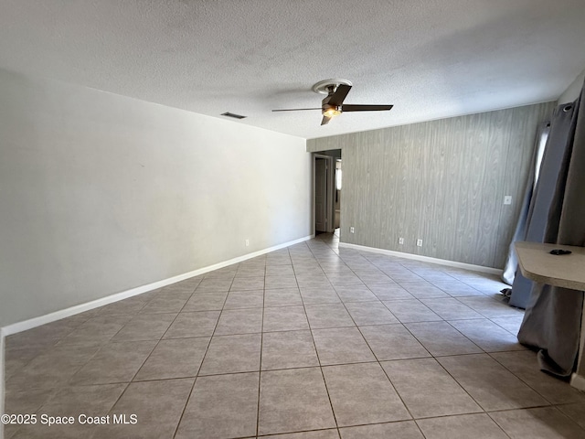 empty room featuring tile patterned floors, a ceiling fan, visible vents, and a textured ceiling