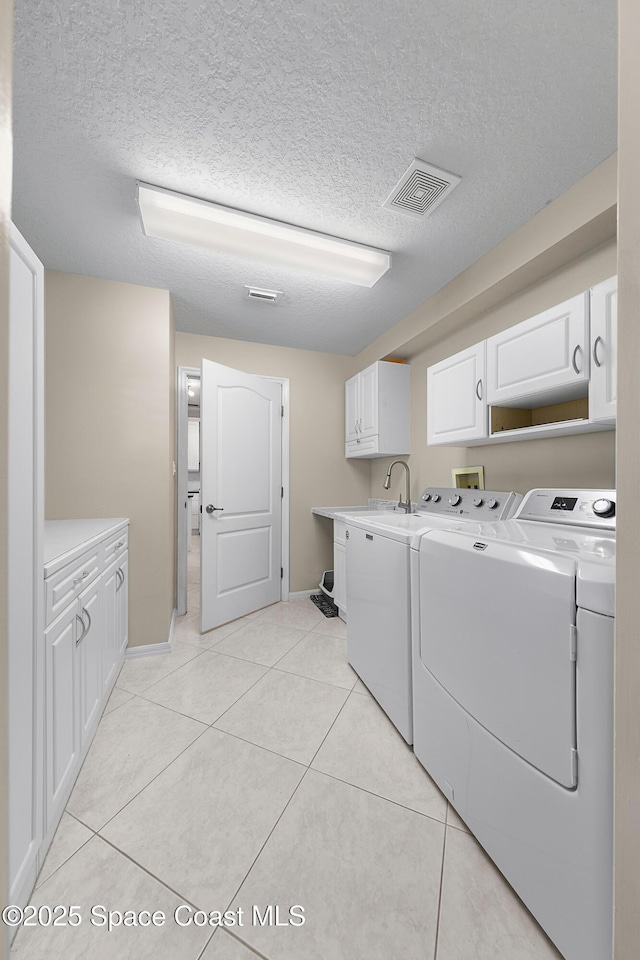 laundry room featuring light tile patterned floors, visible vents, separate washer and dryer, cabinet space, and a textured ceiling