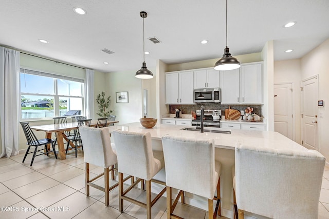kitchen with a kitchen island with sink, a sink, tasteful backsplash, stainless steel appliances, and white cabinets