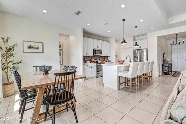 kitchen with a center island with sink, a kitchen breakfast bar, white cabinetry, appliances with stainless steel finishes, and light tile patterned flooring